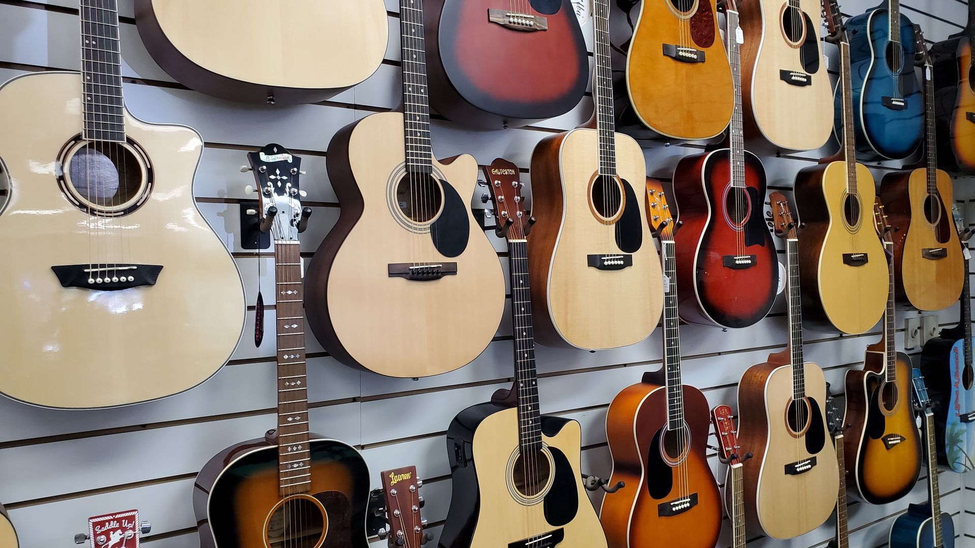 A wall full of acoustic guitars of different sizes and colors