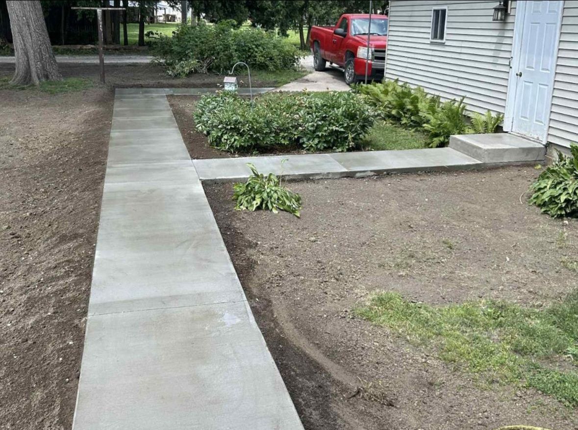 A concrete walkway leading to a house with a red truck parked in front of it.