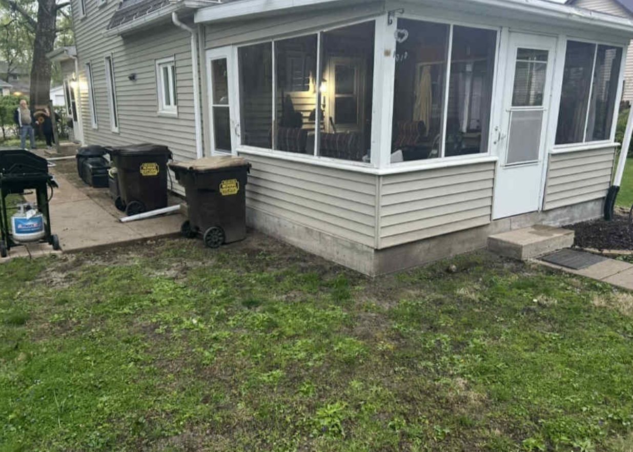 A house with a screened in porch and trash cans in front of it.