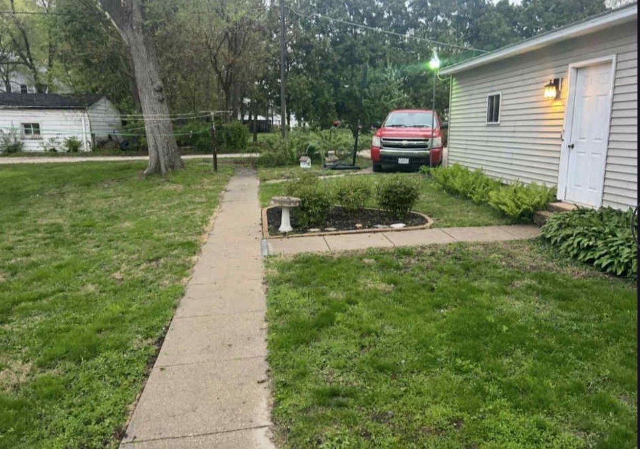 A red truck is parked in front of a house next to a sidewalk.