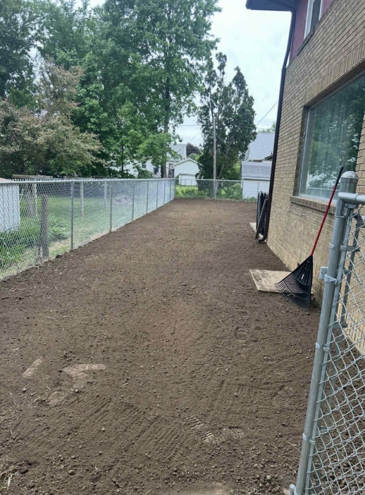 A backyard with a chain link fence and a shovel in the dirt.