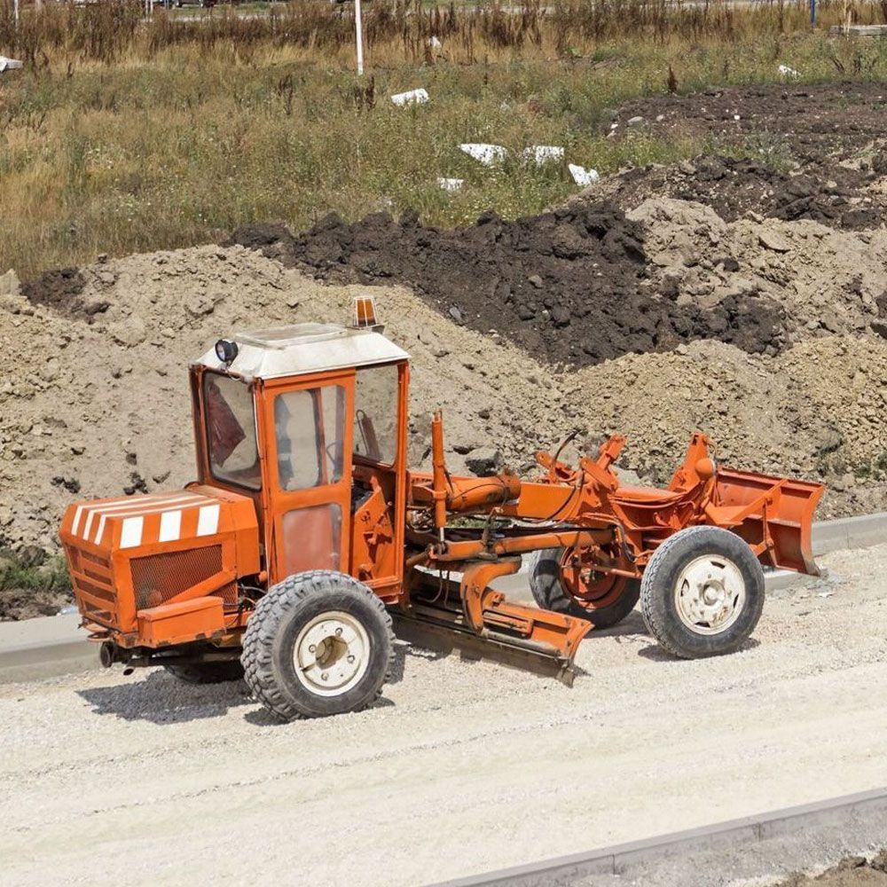 An orange tractor is driving down a dirt road.