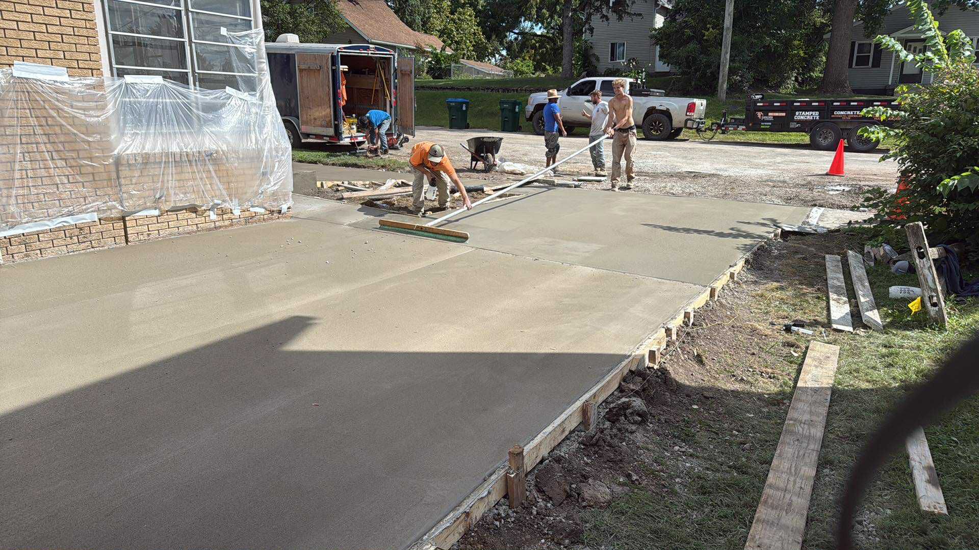 Workers pouring and smoothing fresh concrete on a driveway, brick house in the background.