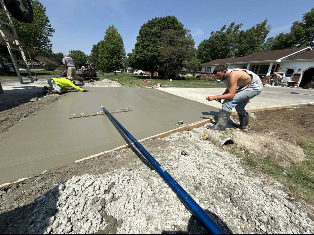 Workers pouring and smoothing concrete driveway on a sunny day.