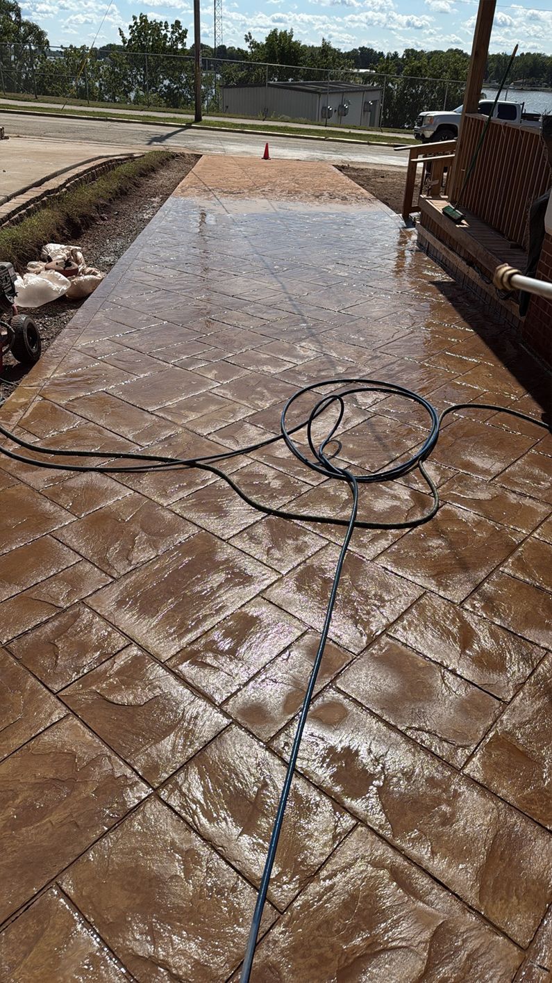 Stamped concrete driveway with water pooling, hose coiled, brown tones.