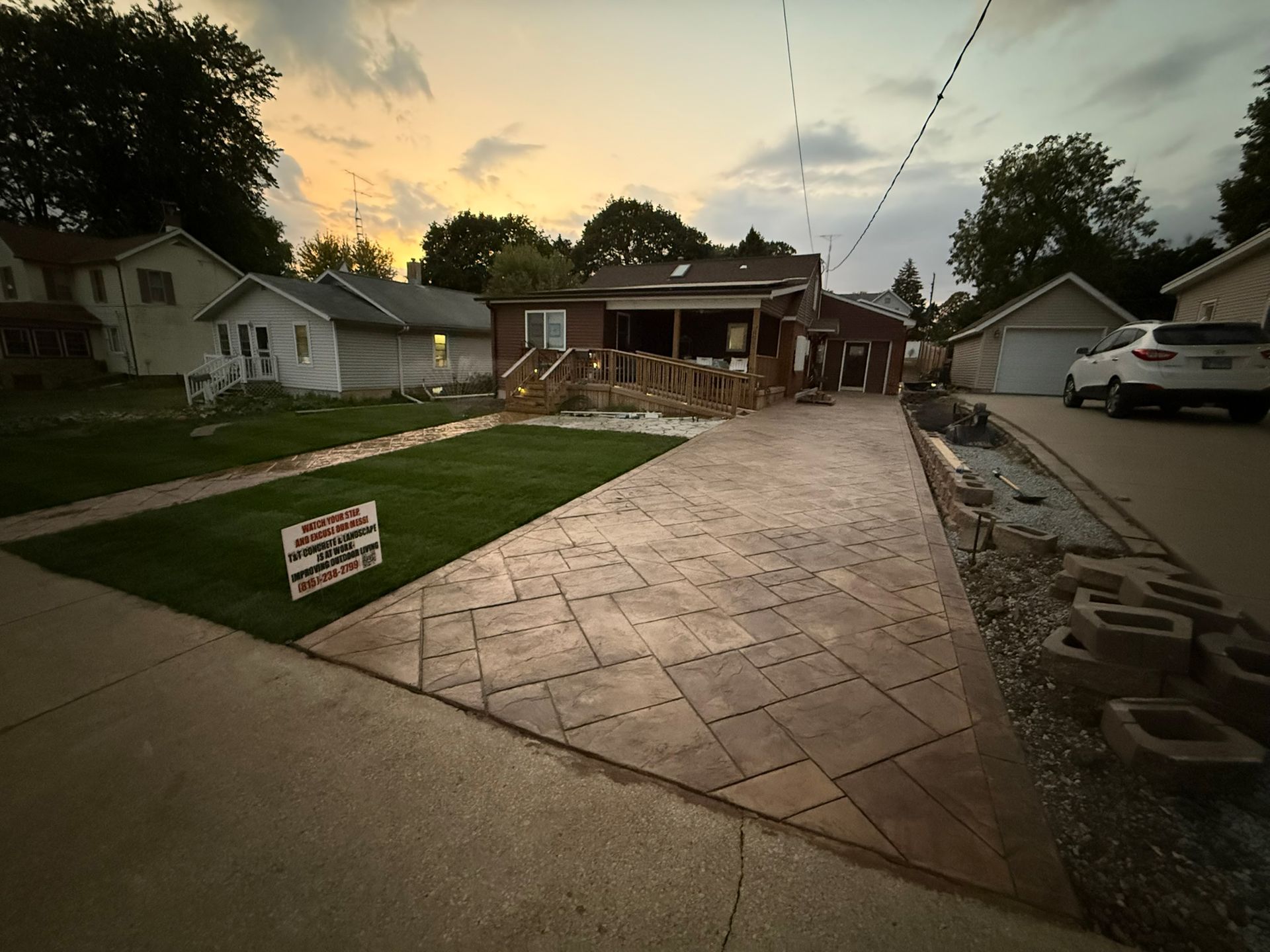 Driveway with stamped concrete leading to a house, flanked by grass and a retaining wall. Dusk sky.