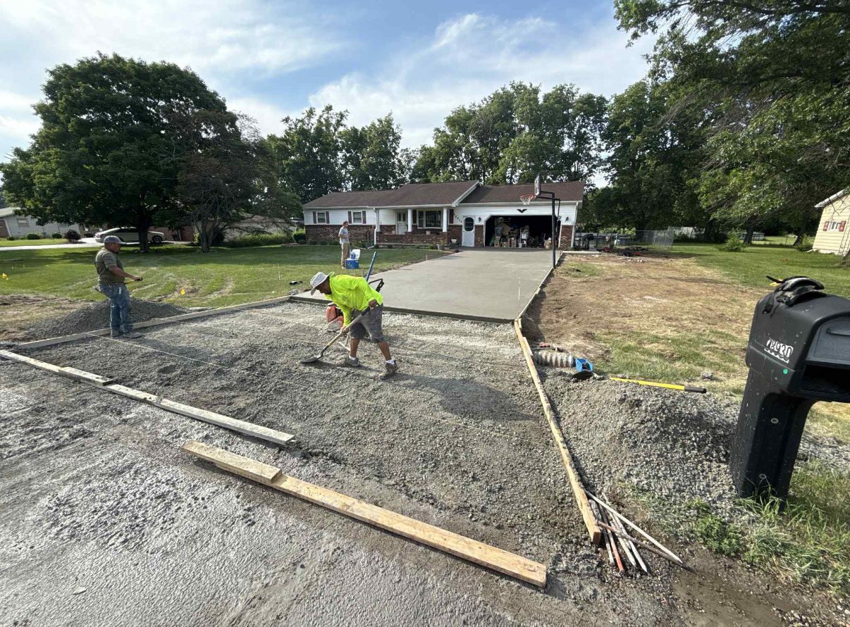 Workers pouring concrete for a driveway in front of a house on a sunny day.