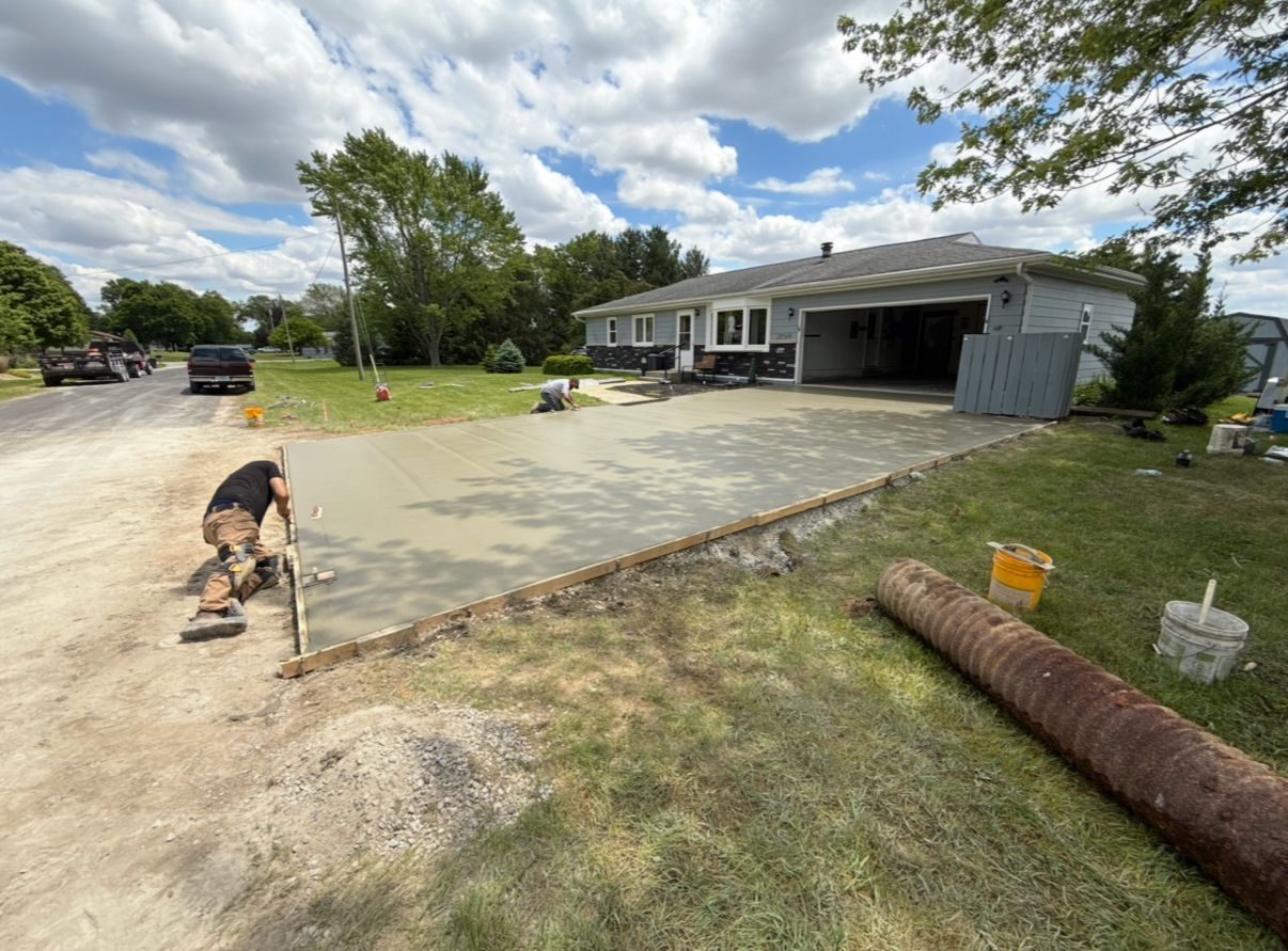 Man leveling fresh concrete driveway in front of a house.