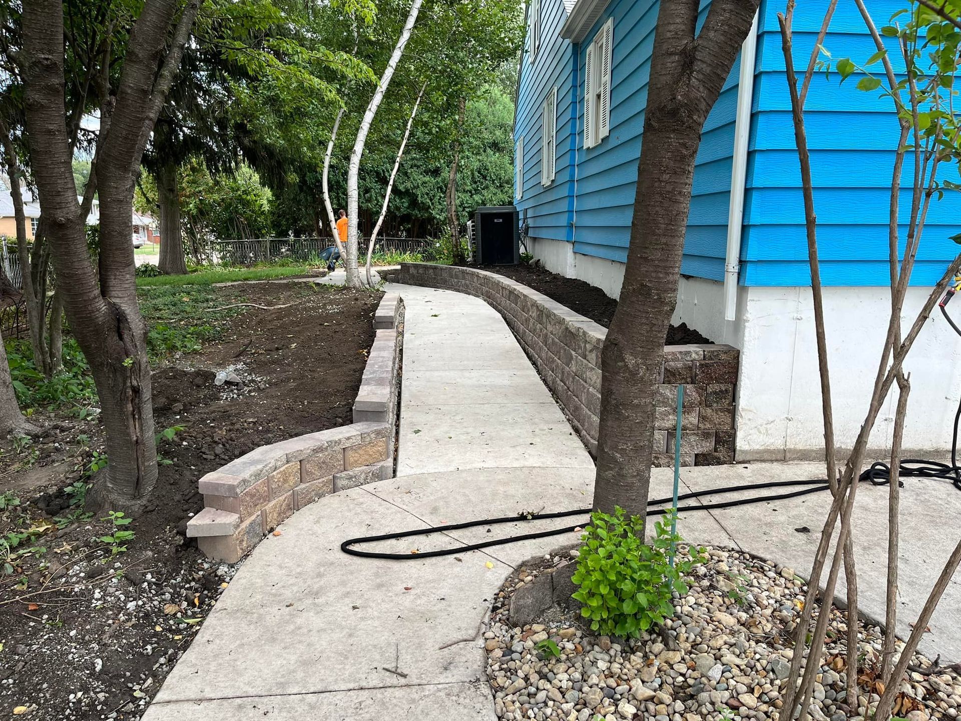 A concrete walkway leading to a blue house surrounded by trees.