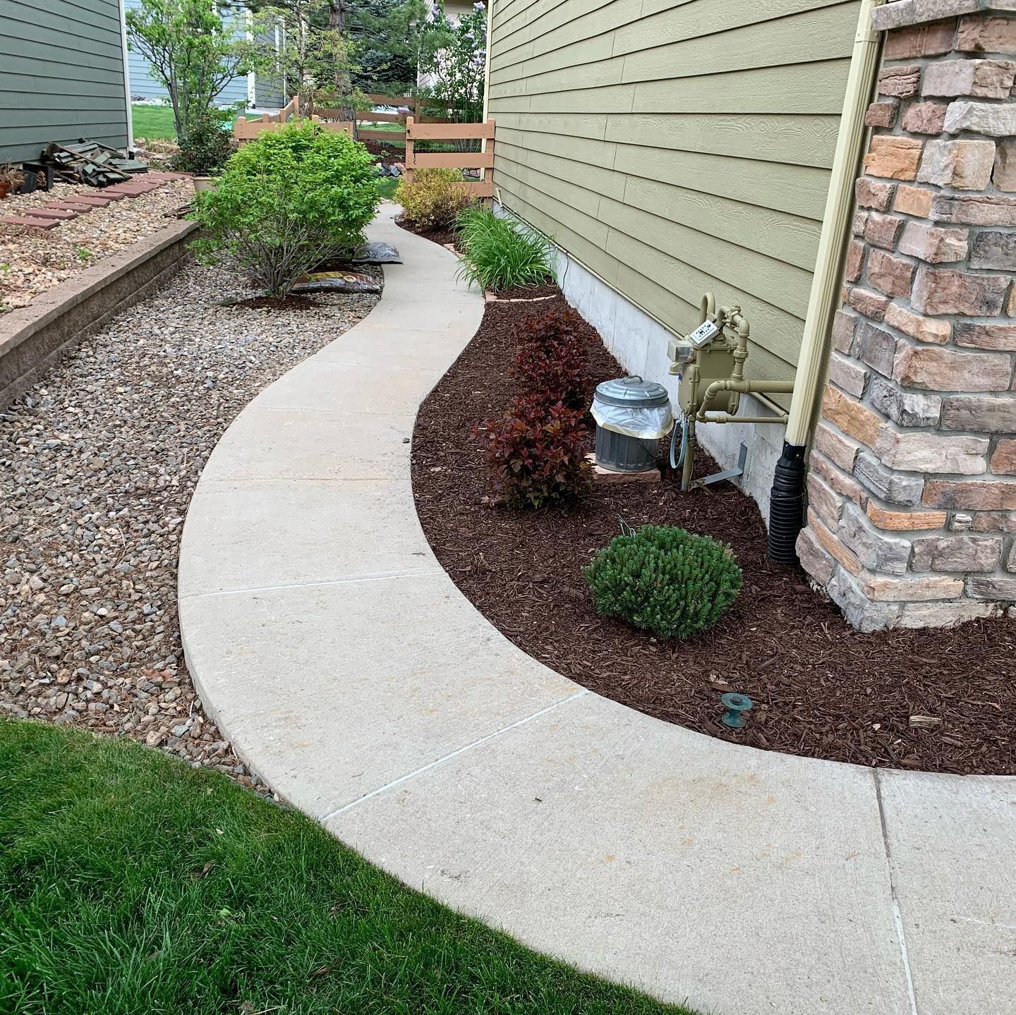 A walkway leading to the side of a house surrounded by mulch and rocks.