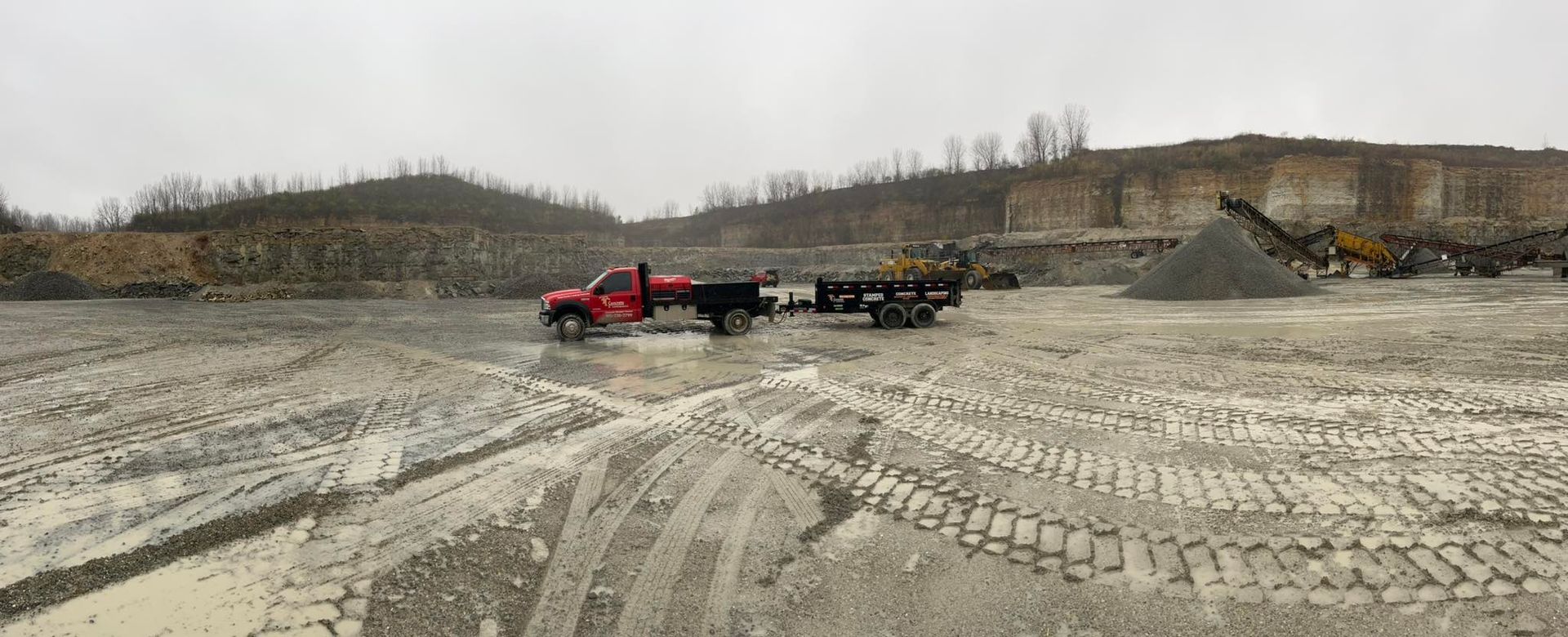 A red truck is pulling a trailer in a dirt field.