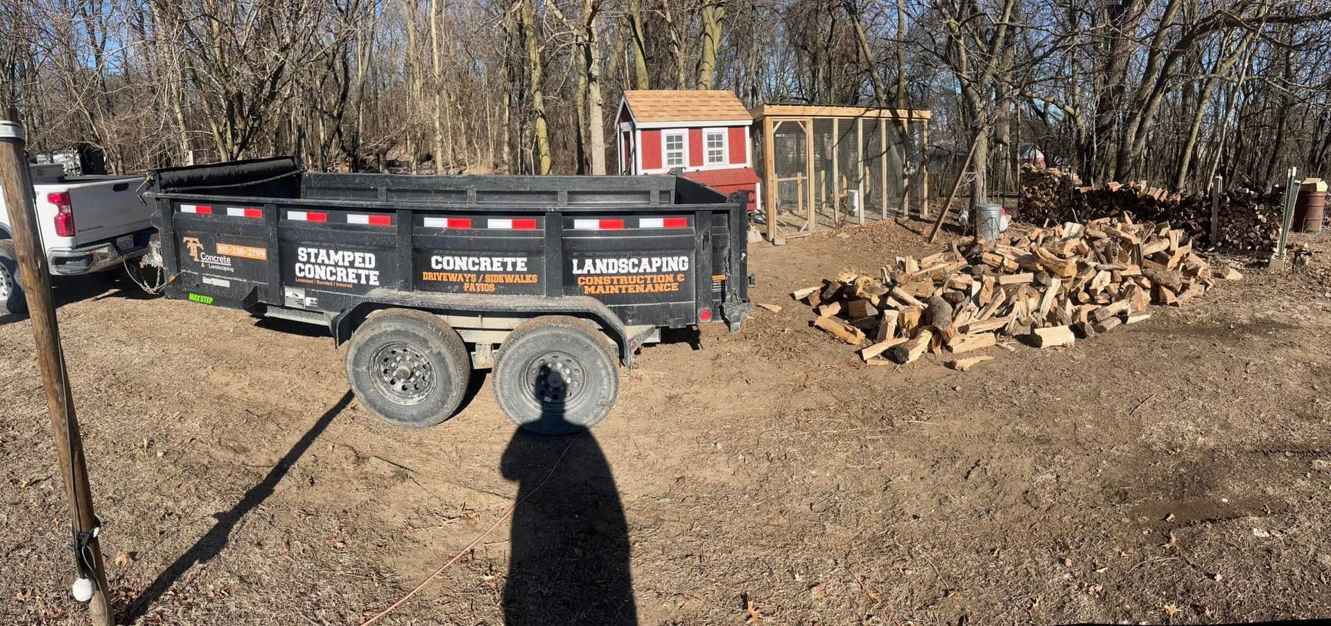 A dumpster is parked in a dirt field next to a pile of wood.