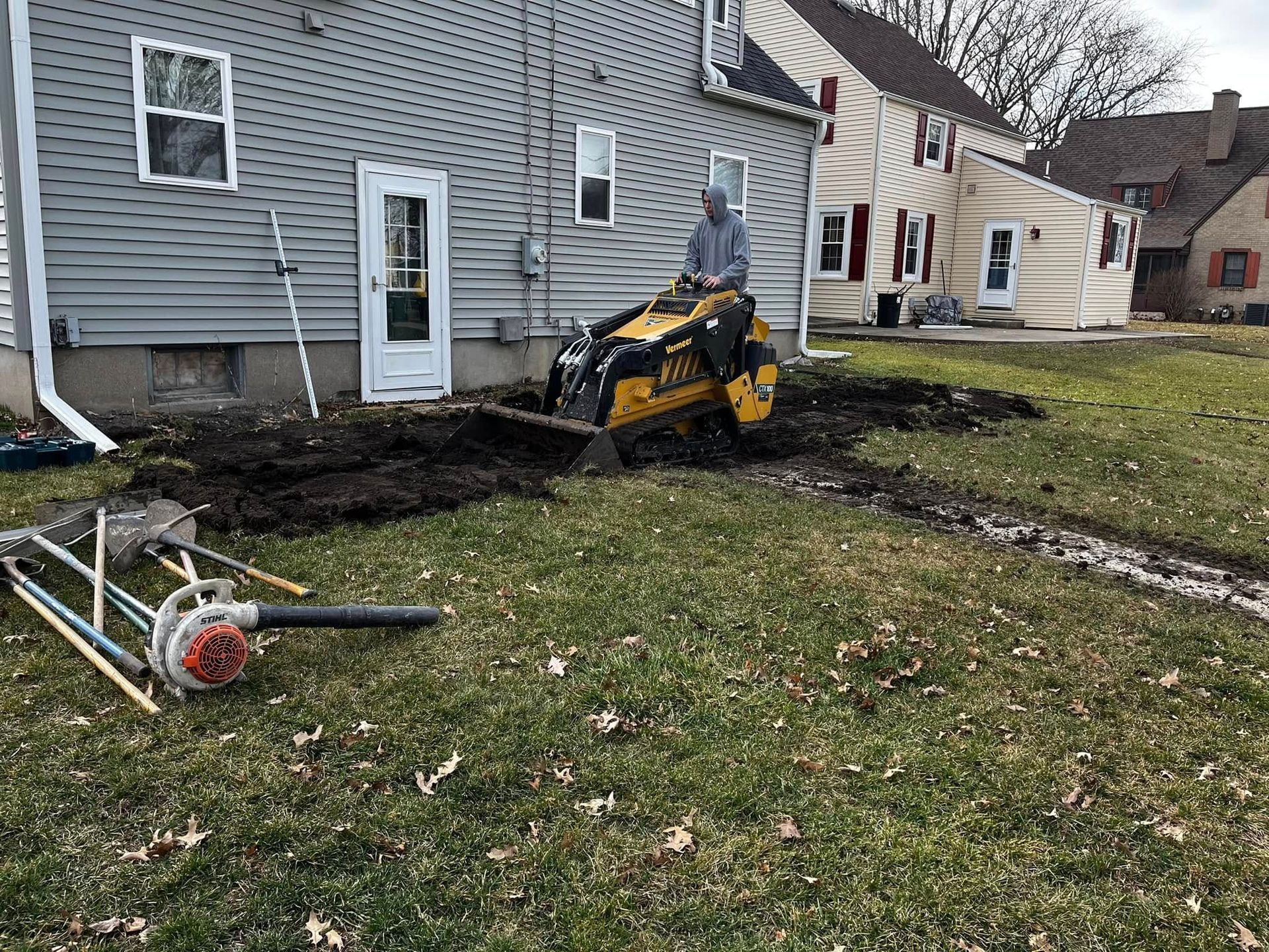 A man is riding a tractor in a yard in front of a house.
