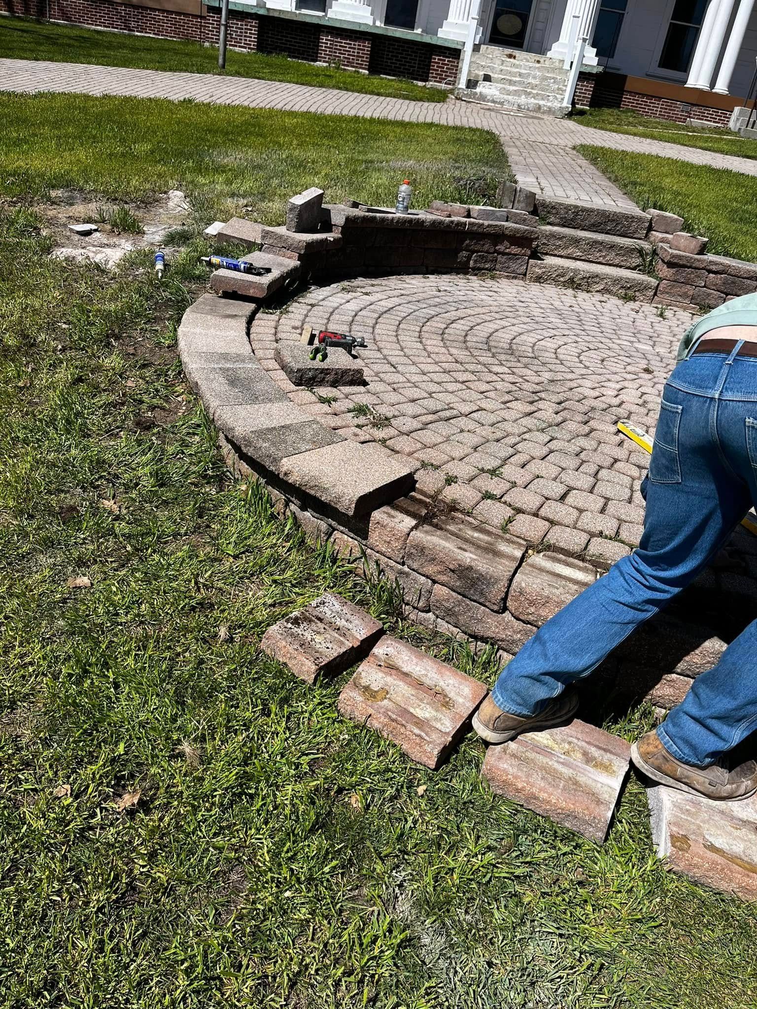A man is laying bricks on a patio in a yard.