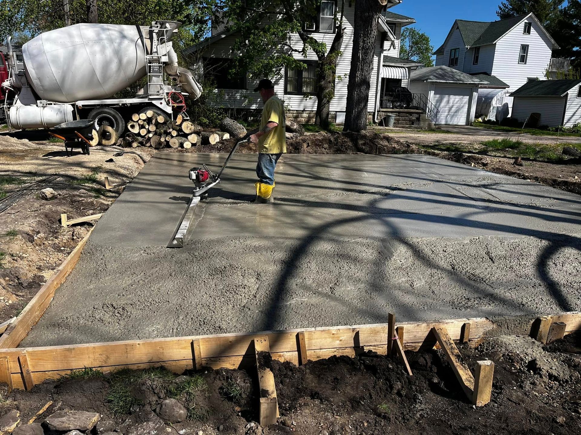 A man is working on a concrete driveway in front of a cement truck.