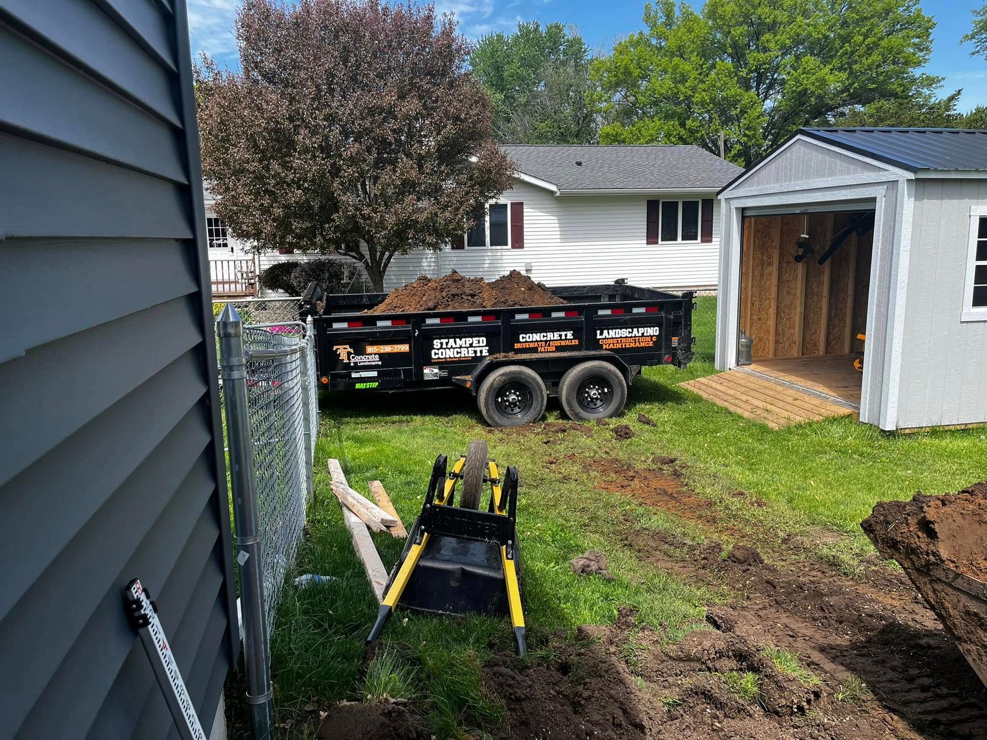 A dumpster is sitting in the grass next to a shed.