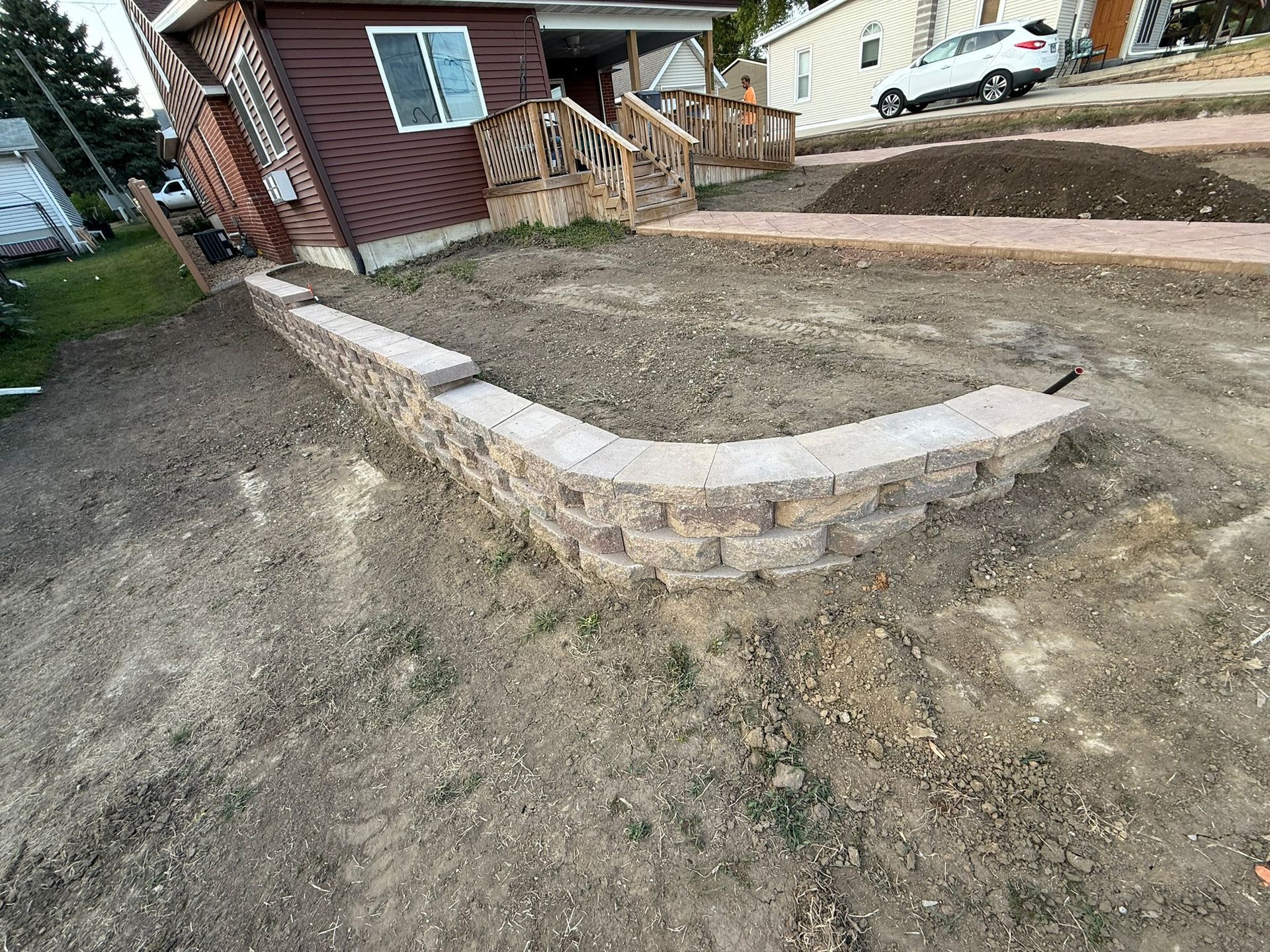 Low retaining wall made of stacked stone blocks in front of a house, surrounded by dirt and unfinished landscaping.