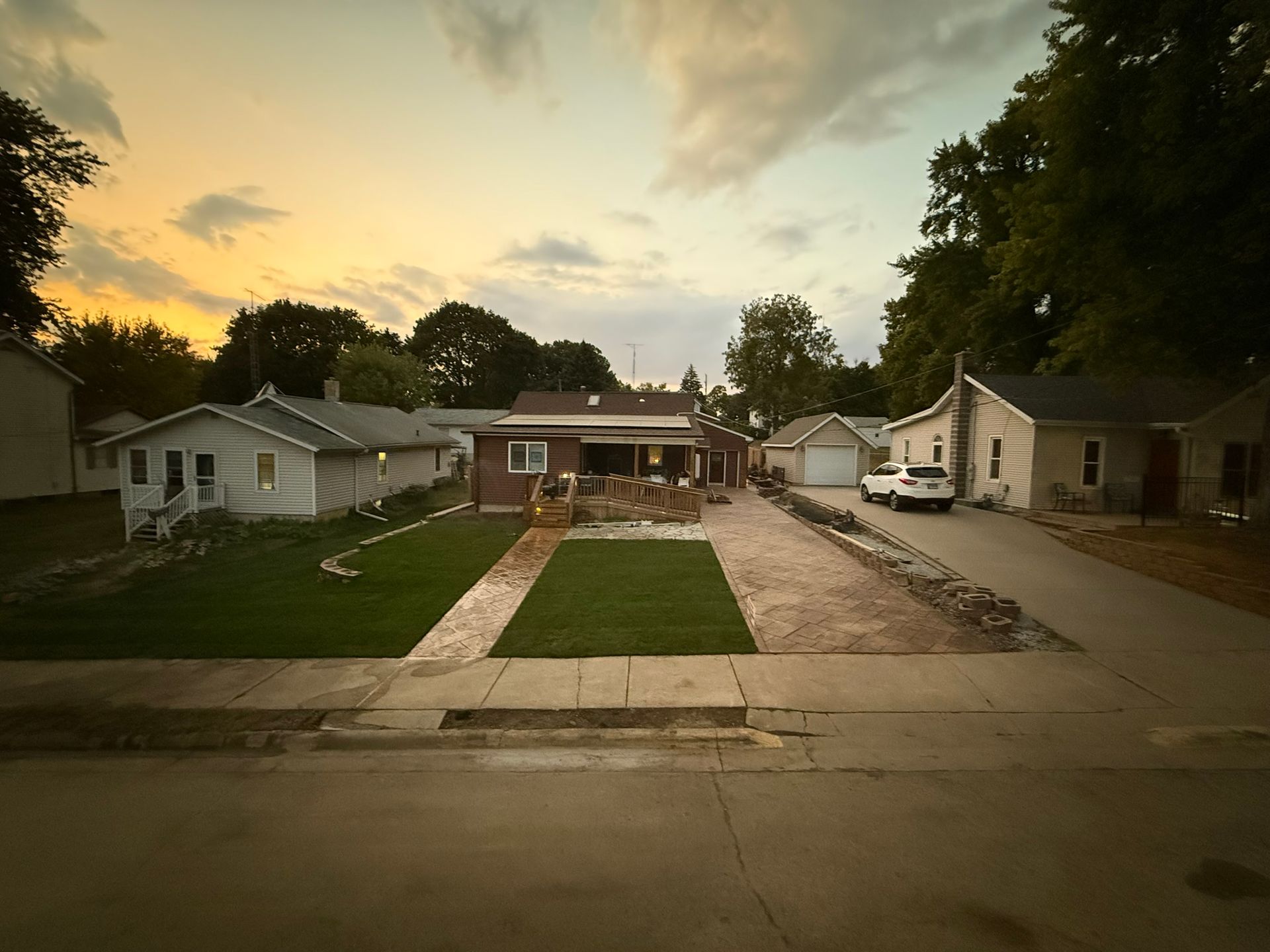 Houses with yards and gravel driveway along a street at dusk; cloudy sky.