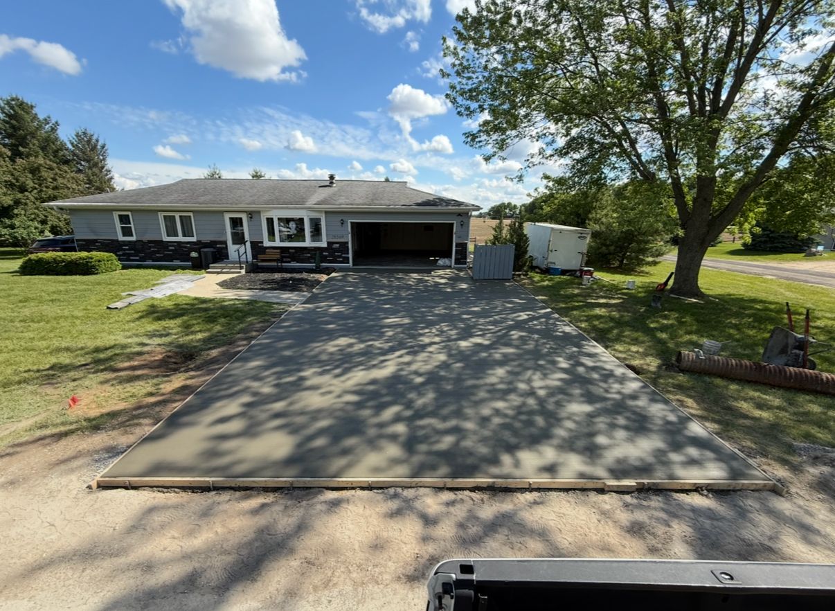 Newly poured concrete driveway in front of a ranch house on a sunny day.