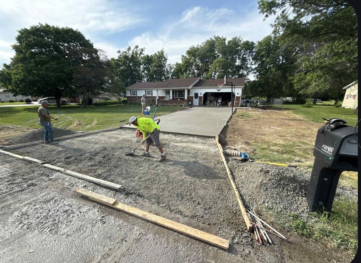 A group of construction workers are working on a concrete driveway in front of a house.