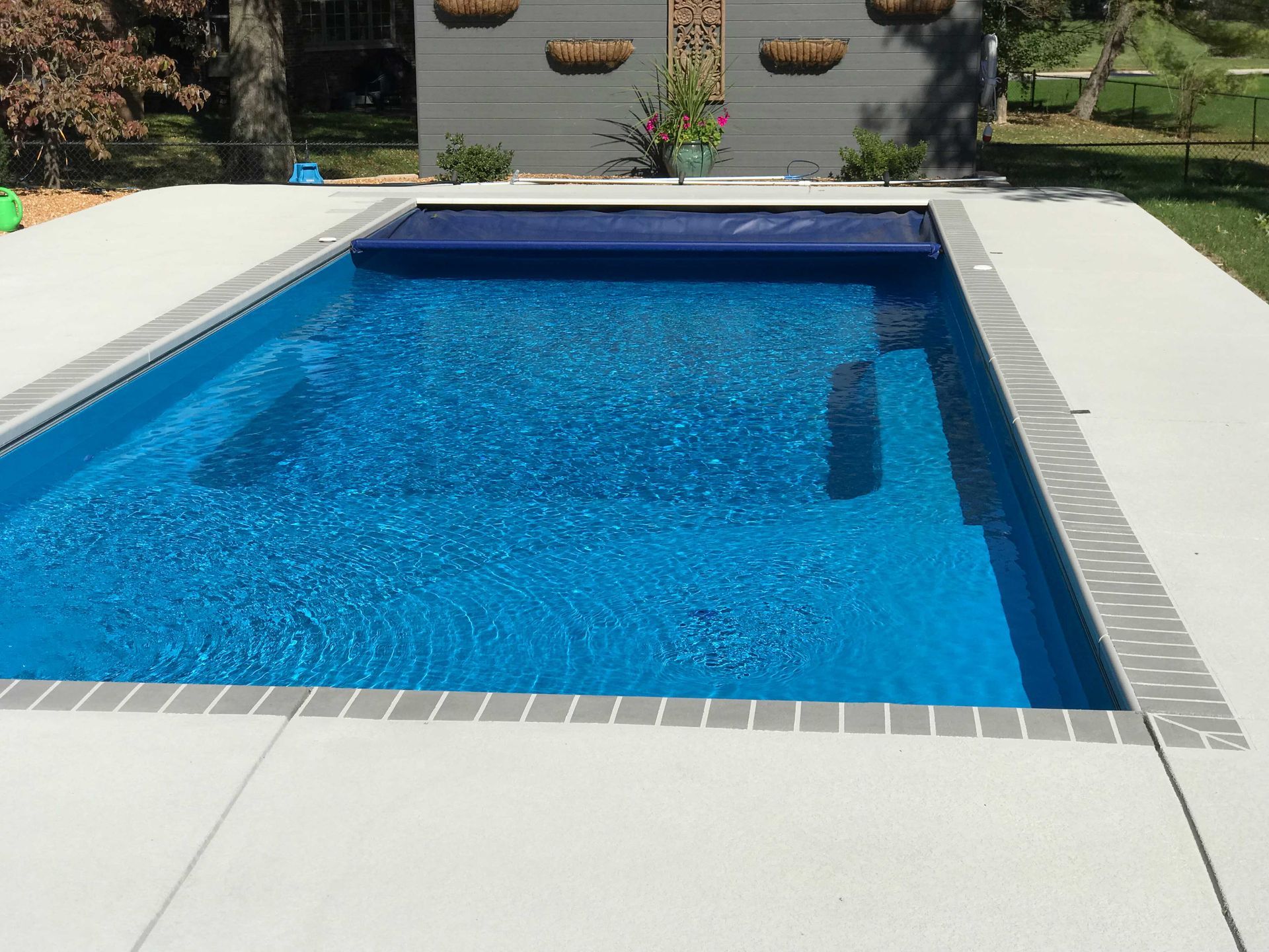Blue rectangular swimming pool with partial blue cover, surrounded by concrete and grass.