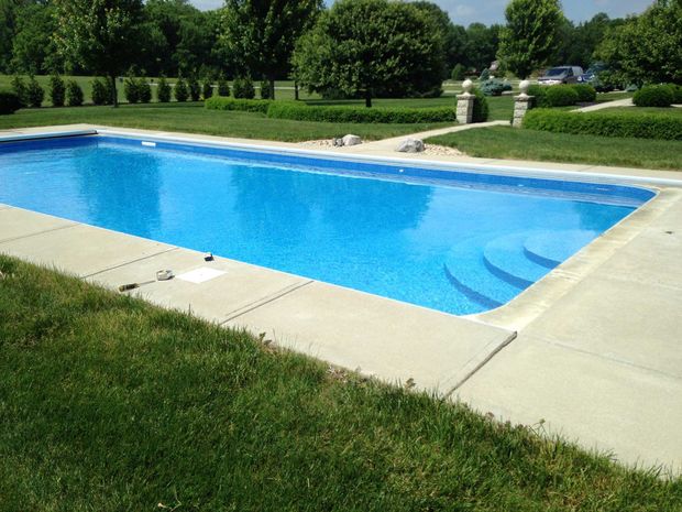 A rectangular swimming pool filled with blue water, surrounded by concrete and green grass.