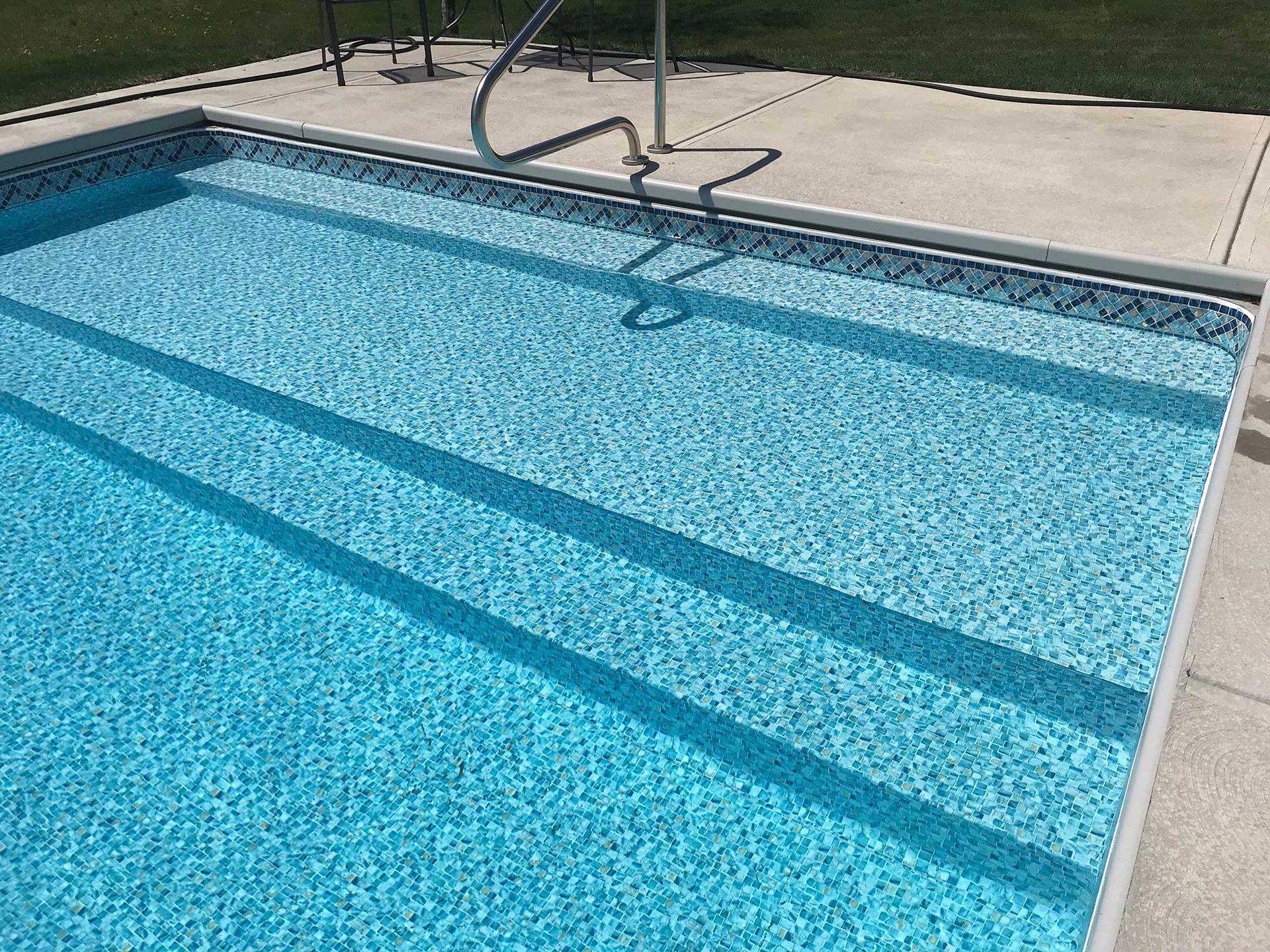 Pool with steps, light blue water, and a stainless steel handrail. Concrete surround.