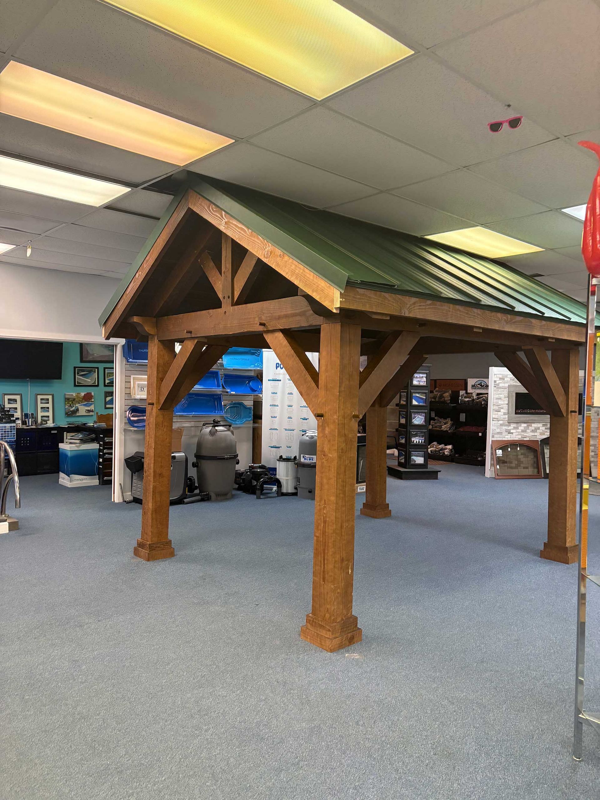 Wooden gazebo with green metal roof in an indoor setting.