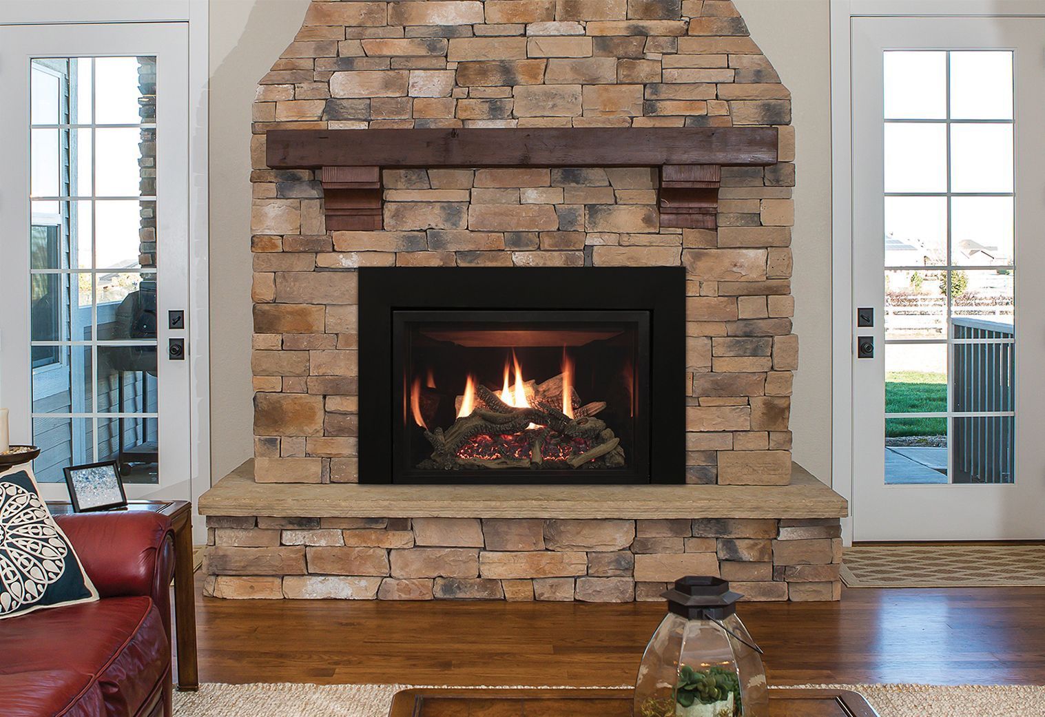 Living room stone fireplace with a burning fire, flanked by glass doors and hardwood floors