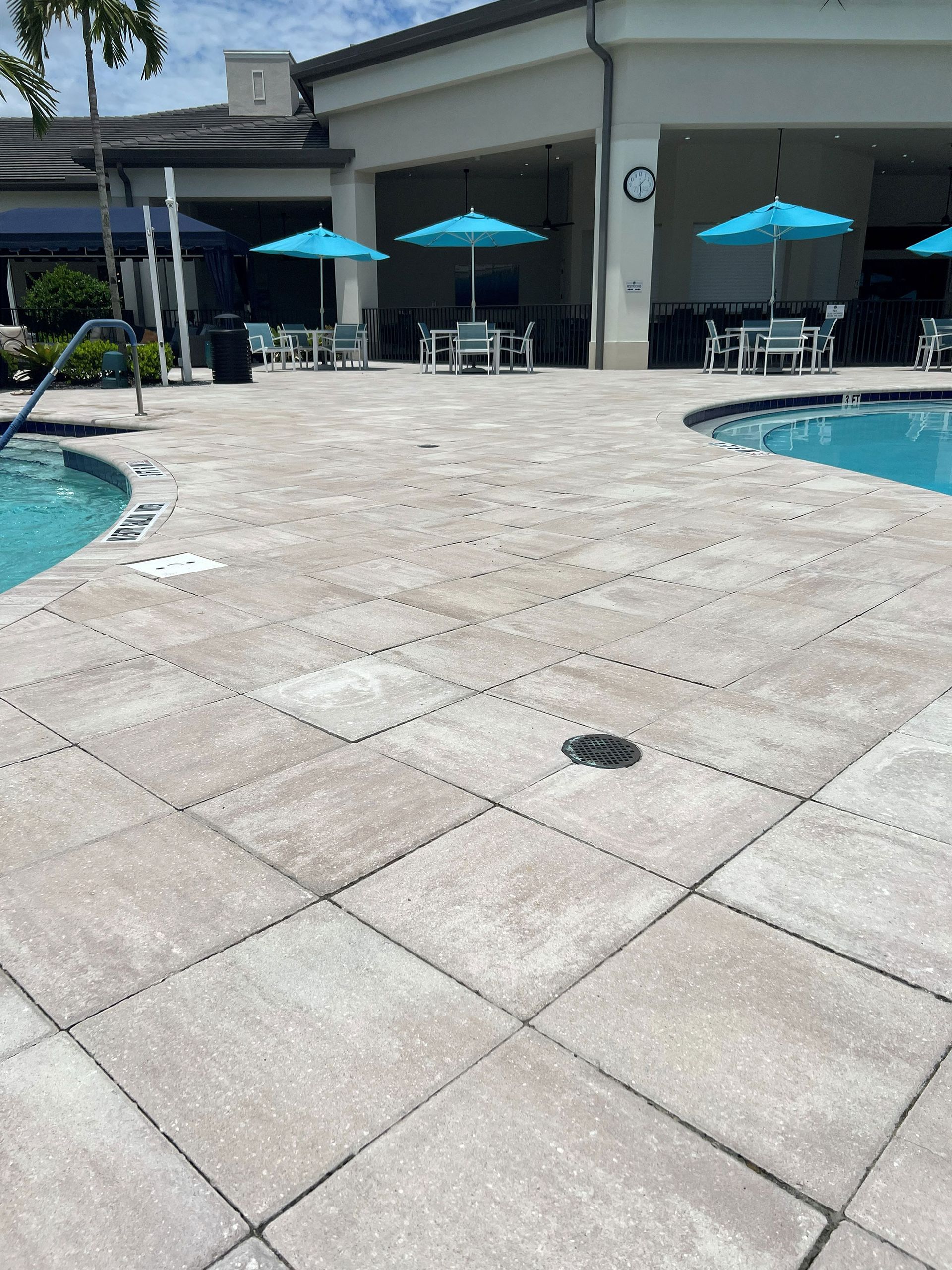 Poolside patio with blue umbrellas, tables, and white building beside swimming pools