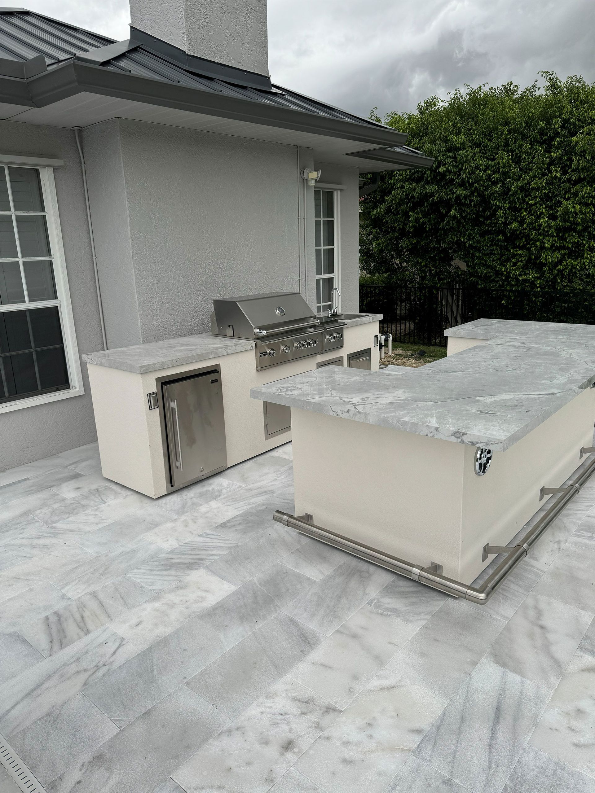 Outdoor patio with gray stone flooring, built-in seating, and a large rectangular fire feature beside a house