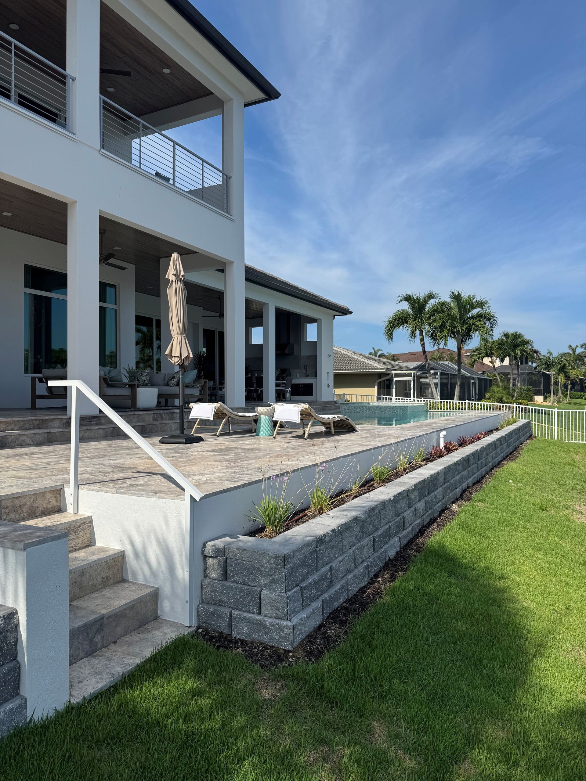 Modern house patio with stone retaining walls, steps, and a grassy yard by the water