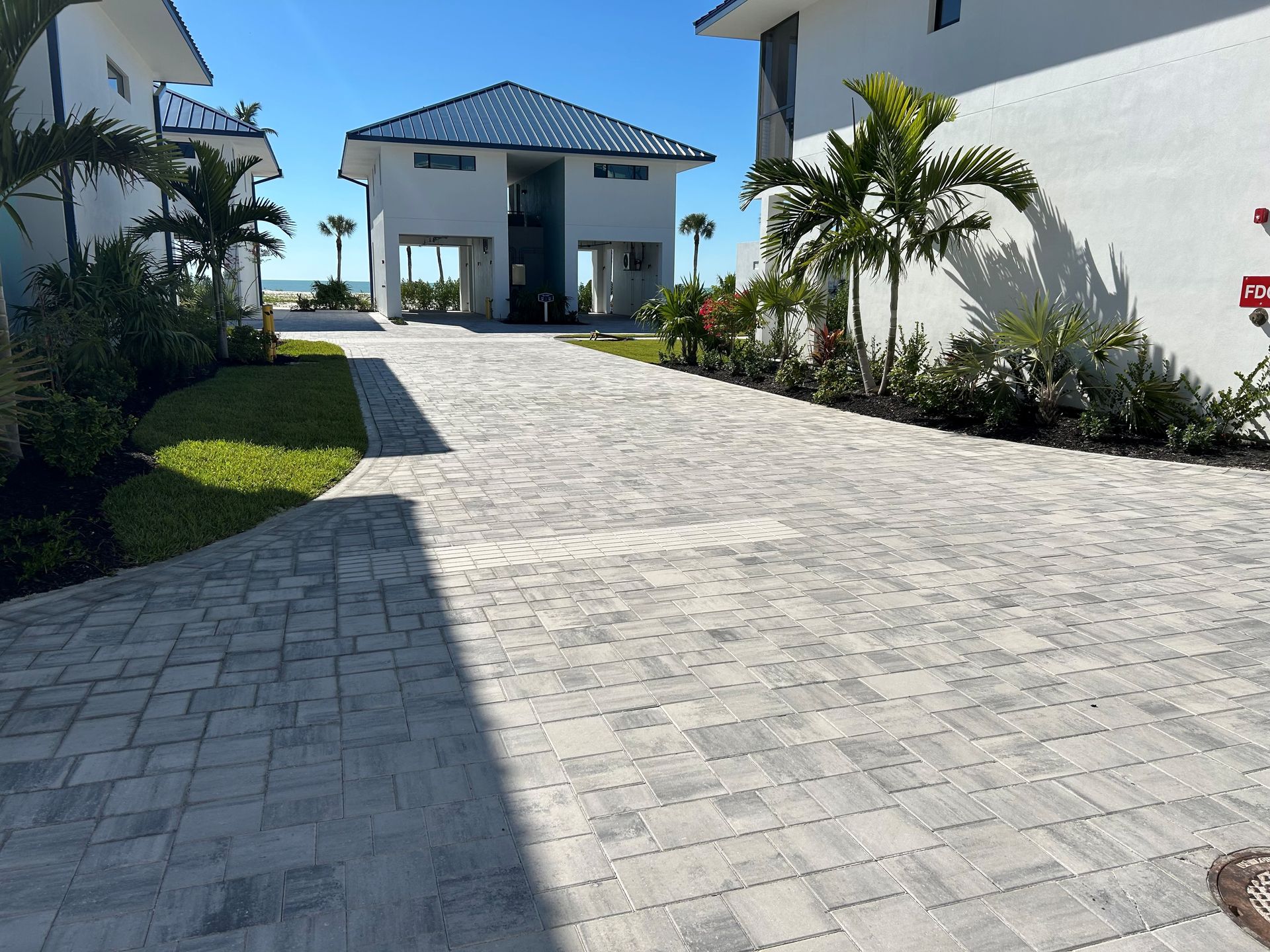 Sunny driveway leading to a white tropical villa with palm trees and a blue roof
