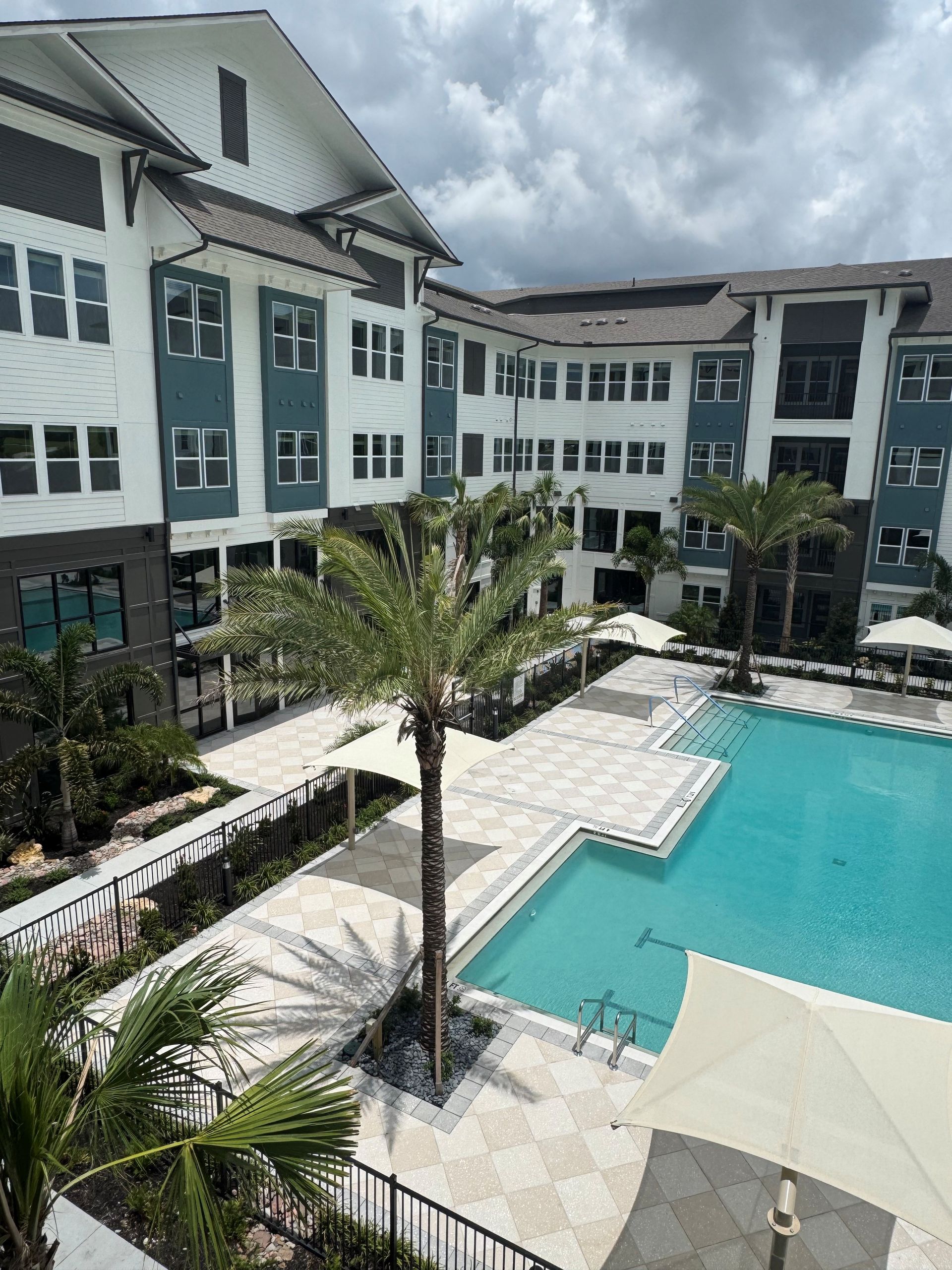 Modern hotel courtyard with turquoise pool, white buildings, and palm trees under cloudy skies