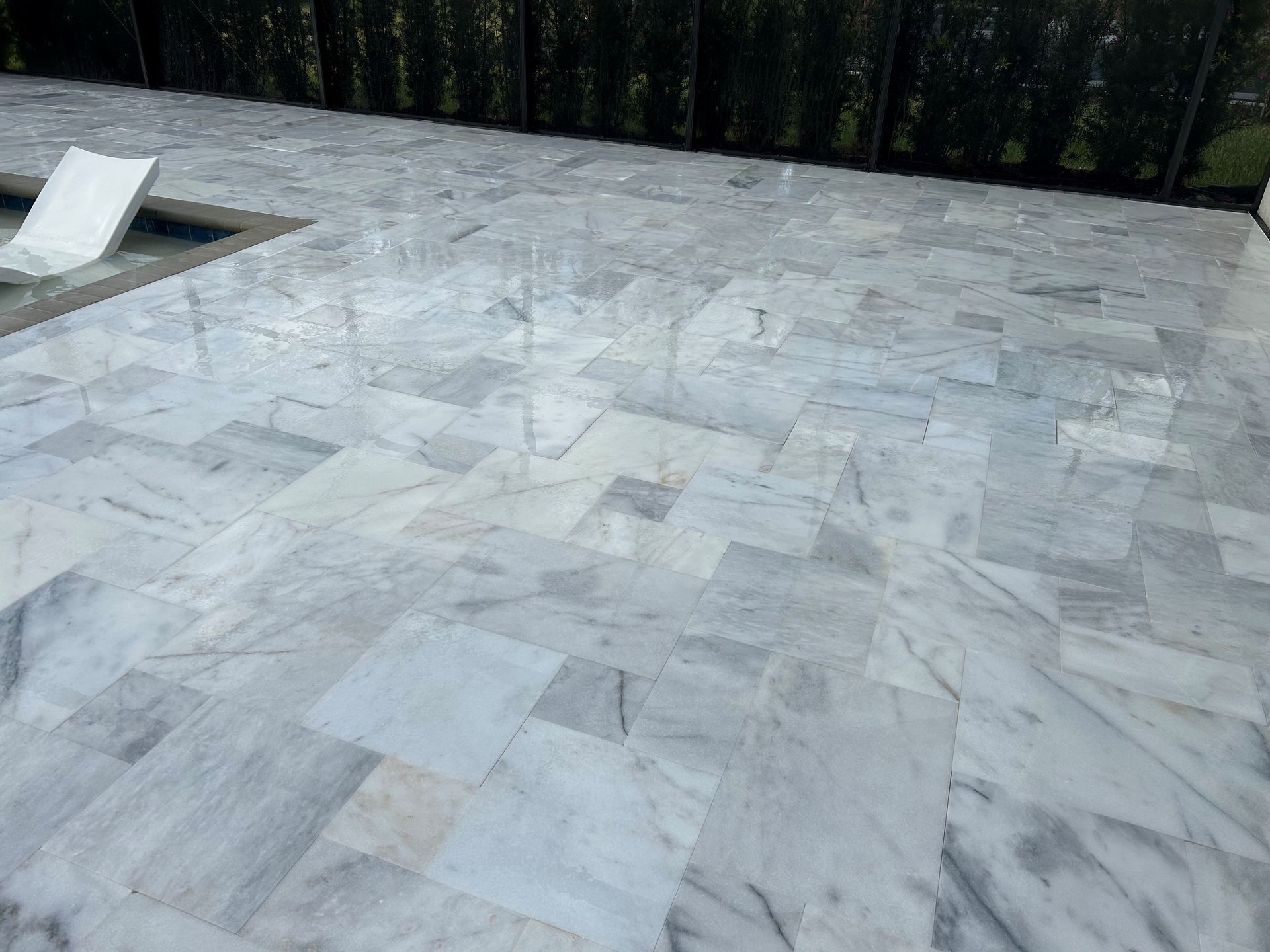 Gray marble-tile patio beside a dark hedge and small white pool edge
