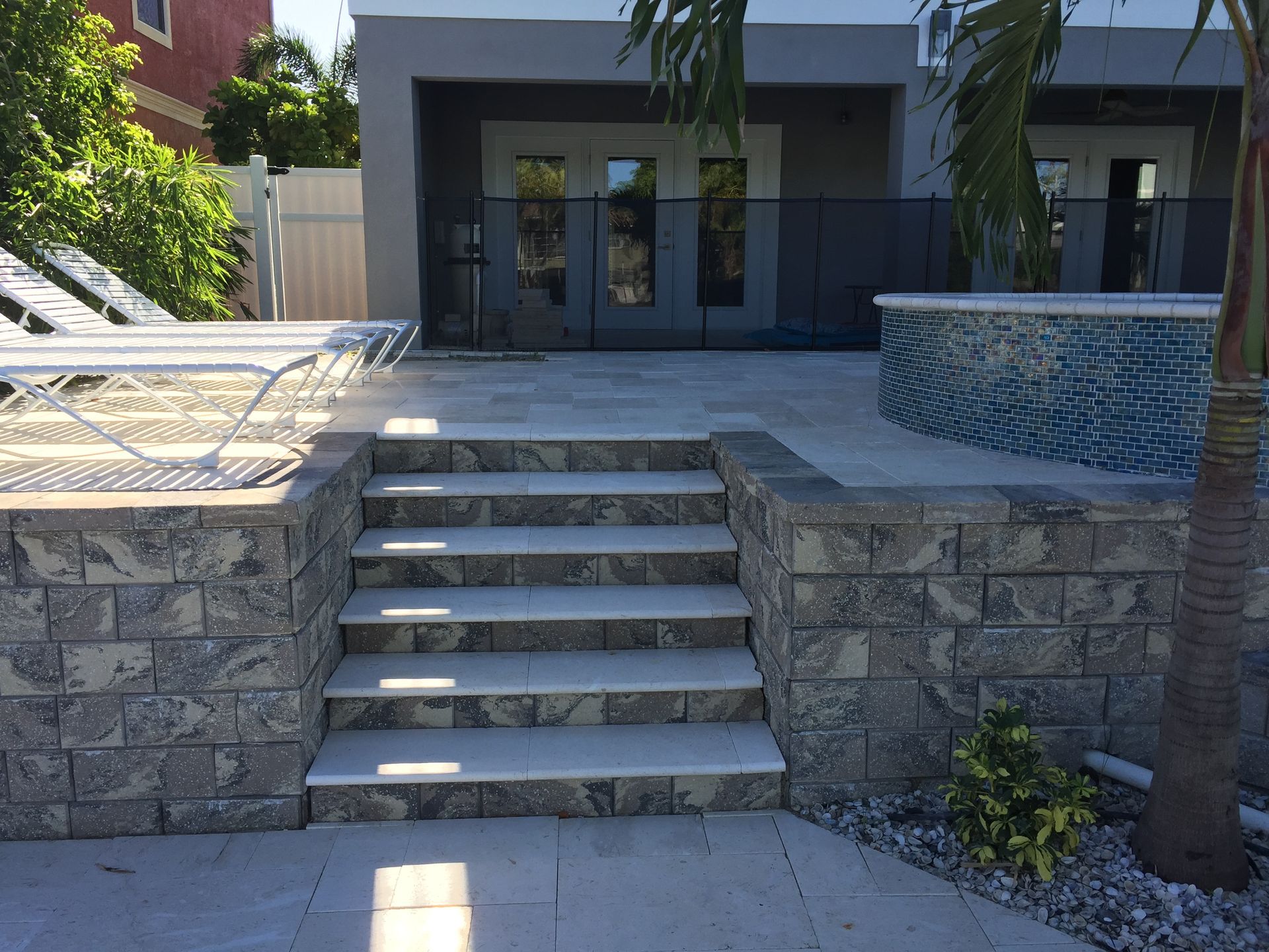 Stone steps leading to a modern building entrance with patio seating and a palm tree nearby