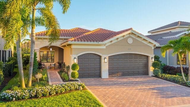 Single-story suburban house with red tile roof, two-car garage, palm trees, and a brick driveway.