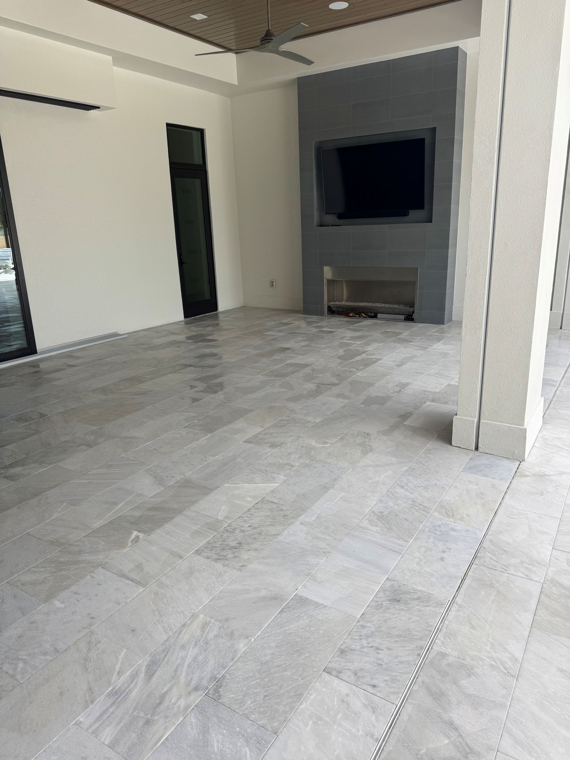 Empty modern living room with gray tile floor, white walls, and a wall-mounted TV above a fireplace.