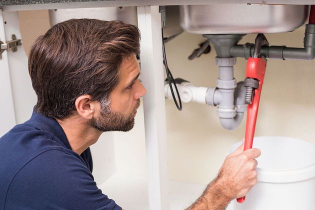Plumber tightening a pipe under a sink with a red wrench in a kitchen cabinet