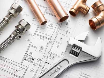Plumbing tools and copper pipes on a blueprint, with a silver wrench in the foreground
