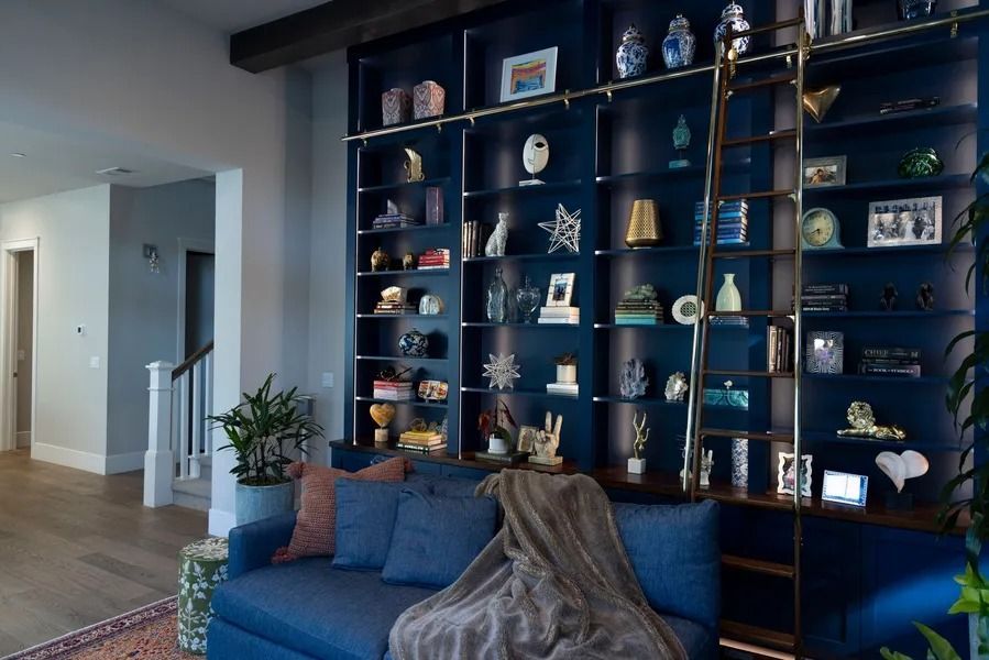 Blue built-in bookshelf with gold ladder, filled with decor, above a blue couch with a throw.