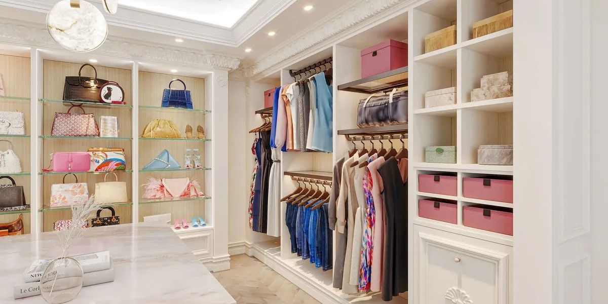Luxury white walk-in closet with handbags displayed and clothing racks. Pink storage boxes.