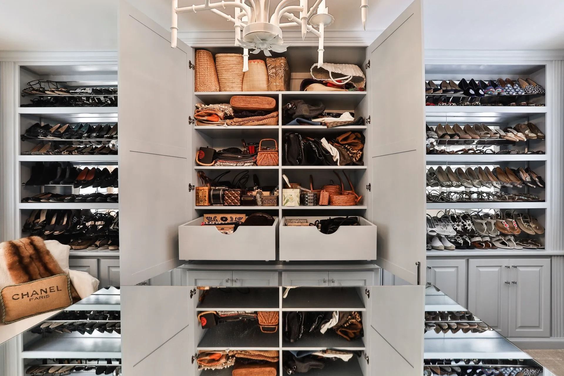 Walk-in closet with shoes and handbags organized on shelves.  Neutral colors, overhead lighting, fur and Chanel bag in foreground.