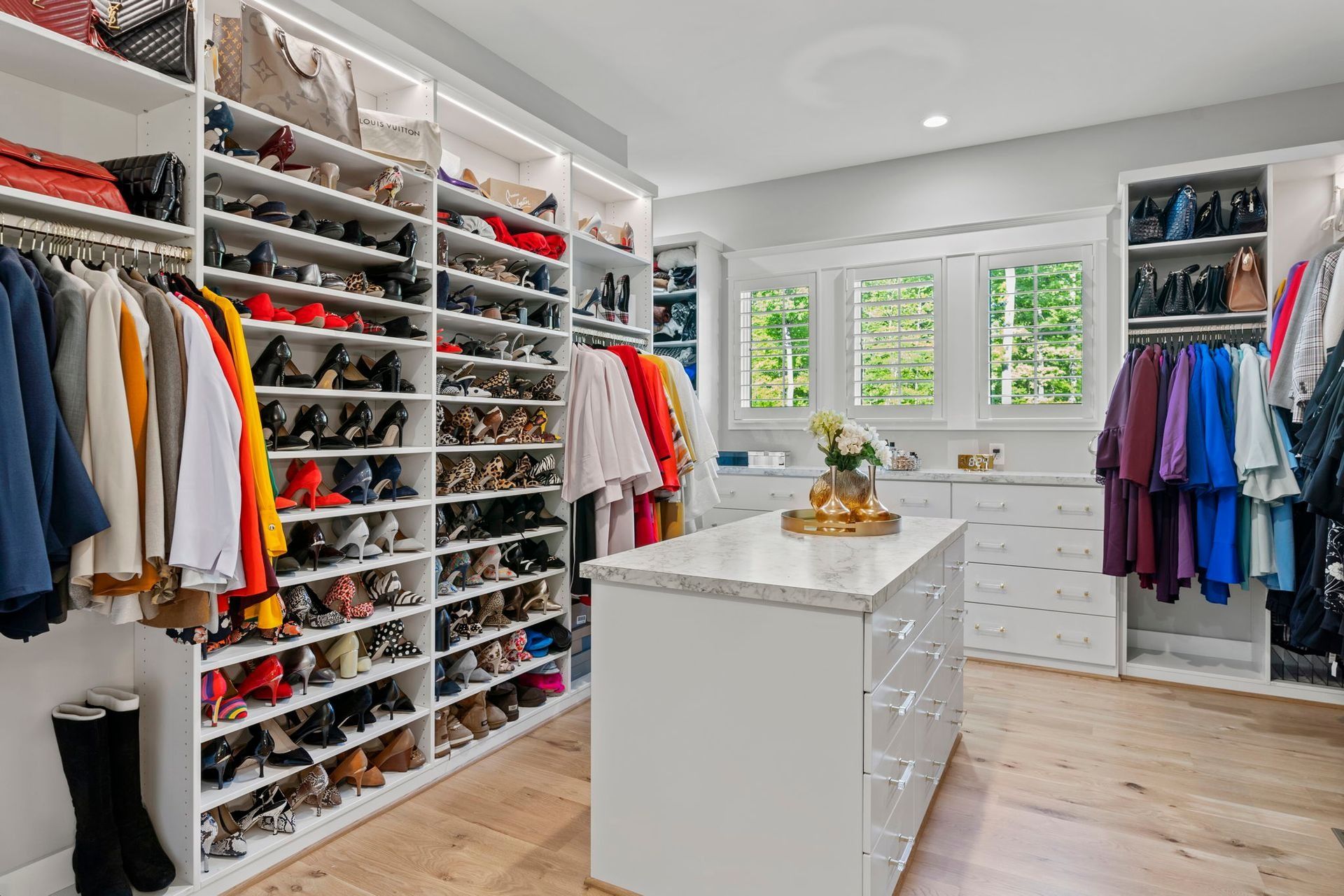 Walk-in closet with white shelves, filled with clothes and shoes, a center island, and natural light.