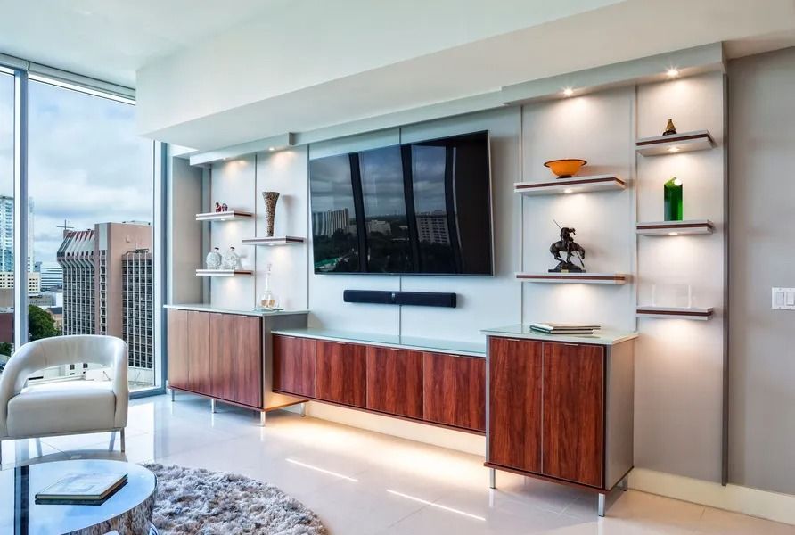 Modern living room with built-in entertainment center, shelves, and large window with city view.