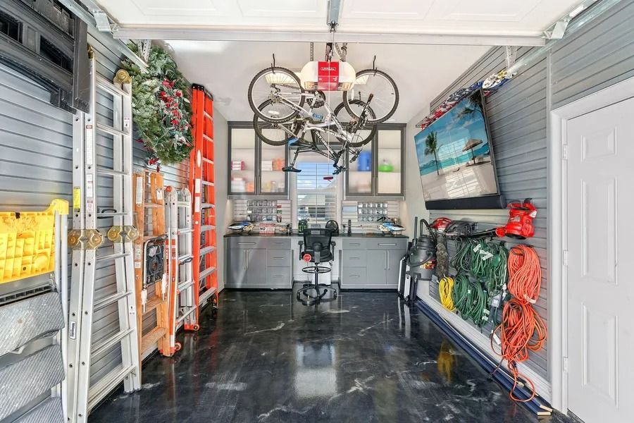 Organized garage with bikes, tools, and storage cabinets, painted gray and with a shiny, black floor.