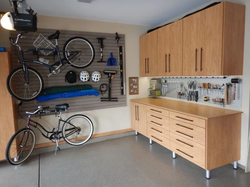 Garage with bike storage, workbench, and tan cabinetry. Bikes on walls, tools on display.
