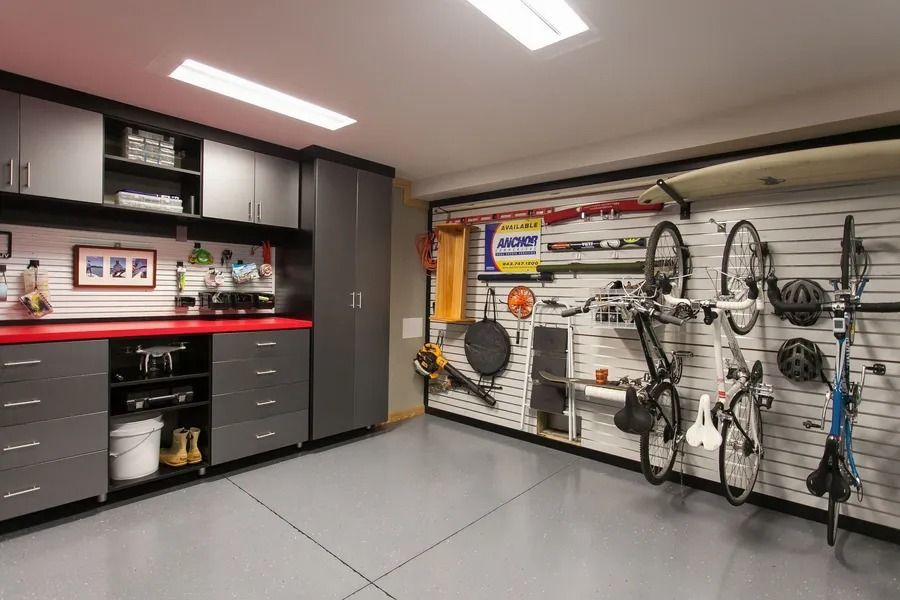Organized garage with gray cabinets, red countertop, and items stored on wall rack; two bikes.