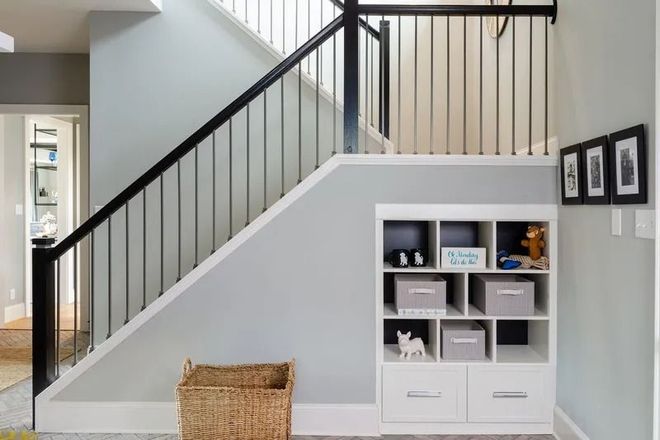 Staircase with black railing, built-in white storage unit, and a woven basket. Light grey walls.