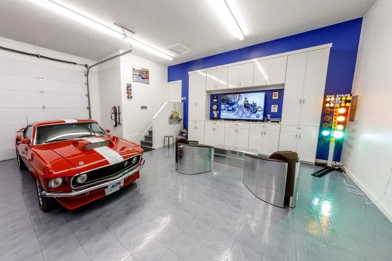 Red Mustang in a luxury garage with a TV, cabinets, and lounge chairs.
